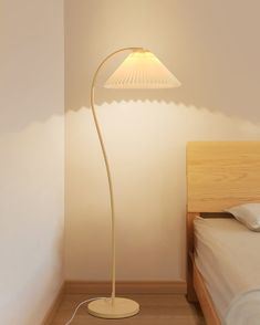 a lamp that is sitting on top of a wooden floor next to a white bed