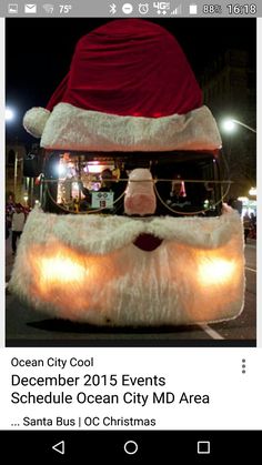 a santa clause bus driving down the street with people standing on it's sides