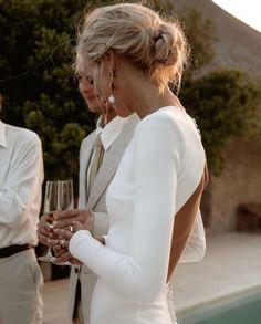 a woman holding a wine glass in her hand while standing next to a man with a suit and tie