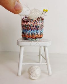 a small white chair with a crochet bag on it and a ball of yarn in front of it