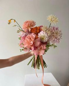 a bouquet of flowers is being held up by someone's hand on top of a table