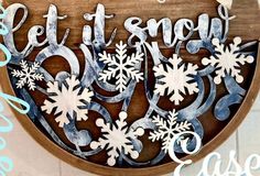 a wooden sign that says let it snow and has snowflakes on the bottom