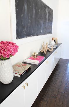 a vase with pink flowers sitting on top of a black counter next to a chalkboard