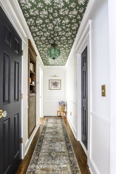 the hallway is decorated with floral wallpaper and green ceiling tiles, along with an antique rug