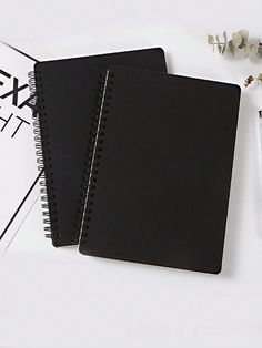 two black notebooks sitting next to each other on top of a white table with flowers