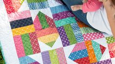 a woman holding a baby on her lap next to a colorful quilt