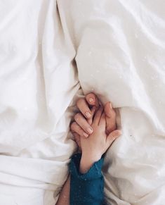 two people holding hands under the covers of a bed