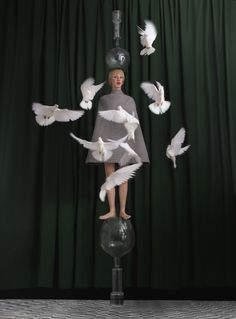 a woman standing on top of a glass ball surrounded by white birds flying around her