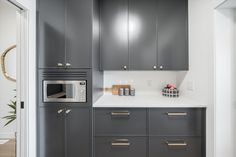 a kitchen with gray cabinets and white counter tops, along with a silver microwave oven