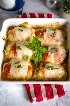 a white casserole dish filled with meat and cheese covered in fresh basil leaves