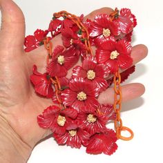 A vintage celluloid red flower necklace. The necklace has a pale red celluloid link chain with a large split ring at one end that loops with the other end of the chain to close the necklace. The necklace is a total of 74 cm long, with the center 58 cm consisting of red pearlescent celluloid flowers wired onto the celluloid chain. The center of every flower, on the other end of the green thread covered wire, is a bunch of small plastic yellow balls glued together.  Each blossom is 3.5 cm across. Orange Vintage Flower Jewelry, Summer Red Flower-shaped Jewelry, Vintage Red Flower Shaped Jewelry, Red Aurora Borealis, Red Flower Necklace, Nolan Miller, Unique Orange Flower-shaped Jewelry, Mermaid Pin, Multicolor Flower-shaped Vintage Jewelry