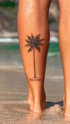 a person standing on the beach with a palm tree tattoo on their leg that says take it easy