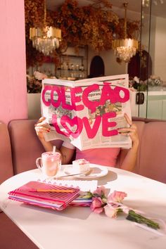 a woman sitting at a table holding up a newspaper with the word colop love written on it