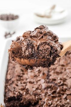 a spoon full of chocolate cake batter being lifted from a casserole dish with a wooden spoon