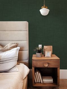 a bedroom with green walls and a nightstand in the corner next to a bed that has two books on it