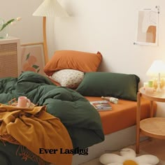 an unmade bed with green and orange sheets in a white room next to a wicker side table