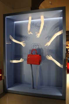 a display case with mannequins holding hands and a red handbag in it