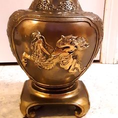 a gold vase sitting on top of a white floor next to a door with an image of a woman riding a horse