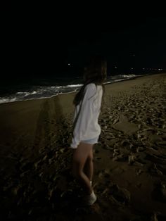 a woman standing on top of a sandy beach next to the ocean under a dark sky