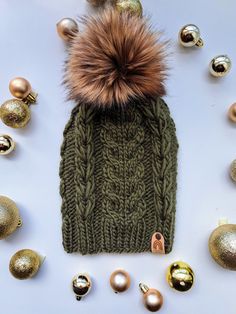 a knitted hat with a fur pom on top surrounded by christmas ornaments and baubles