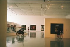 an empty room with people looking at art on the walls