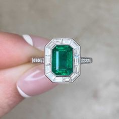 a woman's hand holding an emerald and diamond ring