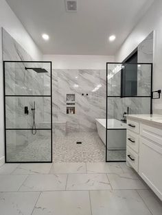 a large bathroom with white marble walls and flooring, along with glass doors leading to the shower area