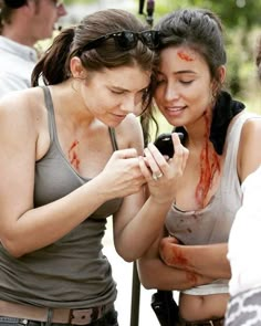 two women with blood all over their face looking at a cell phone while others look on