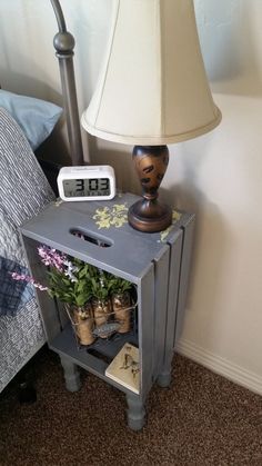 a nightstand with flowers on it next to a night stand and a lamp in the corner