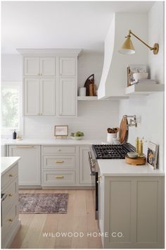 Create a functional yet beautiful kitchen with this white remodel. Featuring a kitchen island with seating and extensive wrap-around cabinets, this space is designed for storage and style. The soft white color palette enhances natural light, while clean lines and warm woods create a cozy atmosphere. Modern lighting and hardware add elegance to complete the look. Learn how the kitchen layout was adjusted for better flow and function, making it perfect for everyday use and family gatherings. White Cabinets Brass Hardware, Greige Kitchen, Elegant Kitchen Design, Custom Range Hood