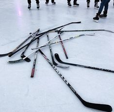 several hockey sticks laying on the ice with people standing in the background looking at them