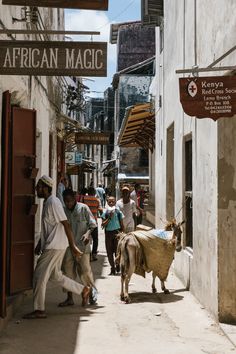 people are walking down an alley way with a cow on the side and a sign above it that says african magic