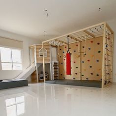 an indoor climbing wall in the middle of a room with white flooring and windows