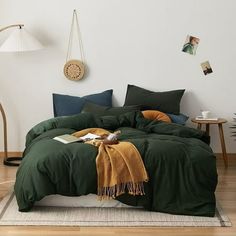 a bed with green sheets and blankets in a room next to a lamp on the wall