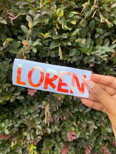 someone holding up a sticker with the word loren on it in front of a bush