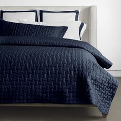 a bed with blue bedspread and white pillows on top of it, next to a wall