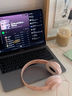 an open laptop computer sitting on top of a white desk next to headphones and a drink