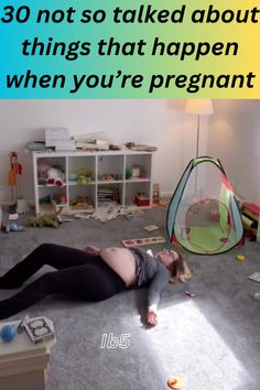 a pregnant woman laying on the floor in front of a child's play tent