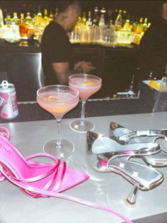 two martini glasses and one pink shoe are sitting on the bar