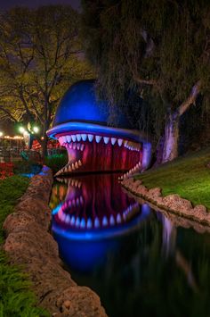 a blue and red sculpture with teeth on it's face next to a body of water