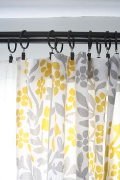 yellow and gray curtains hanging on a rod in front of a window with white drapes