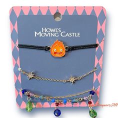 two bracelets with charms on them sitting in front of a card board that says how's moving castle