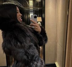 a woman taking a selfie in front of a mirror wearing a fur coat and holding a cell phone