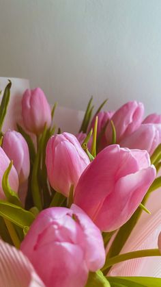 a bouquet of pink tulips sitting on top of a white table next to a wall