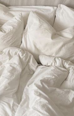 an unmade bed with white sheets and pillows