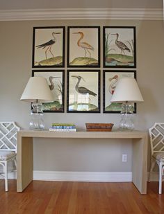 two lamps are sitting on a table in front of four framed pictures with birds above them