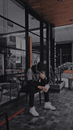 a person sitting on a bench in front of a building with glass windows and plants