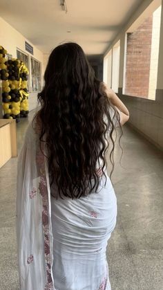 a woman with long hair is walking down the hallway wearing a white sari and holding her hand on her hip