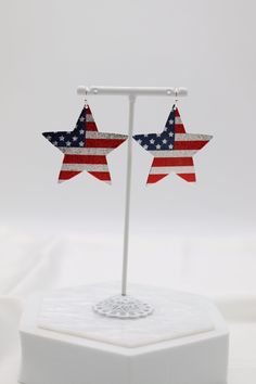 Elevate your style with our Silver Large Sparkle Flag Star Earring. Made from high-quality silver, these earrings are designed to add a touch of elegance to any outfit. The large star shape with sparkling detailing creates a unique and eye-catching look. Perfect for any occasion, these earrings are sure to make a statement wherever you go. Length: 1.94” Width: 1.81” Closure: Fish Hook Material: Zinc, Brass and Steel with Rhodium Plating Lead and Cadmium Safe - It is not Nickel Free Star Charm Earrings For Party, Silver Starburst Earrings For Party, Silver Star Embellished Earrings For Party, Silver Star-shaped Earrings, Red Dangle Earrings For 4th Of July, Cheap Red Patriotic Earrings, Red Star Charm Earrings, Adjustable Red Patriotic Earrings, Red Star-shaped Earrings With Star Charm