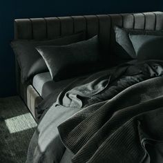 an unmade bed with black linens and blankets on it in a dark room